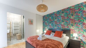 Un dormitorio moderno con una cama grande, un papel tapiz tropical y un ventanal de vidrio que da a un balcón.