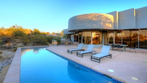A modern pool area with lounge chairs and a pool, surrounded by a building with large windows.