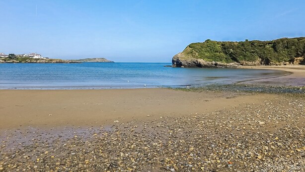 Una playa de canto rodado con aguas azules cristalinas, una orilla arenosa y un acantilado rocoso con vegetación.