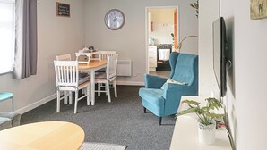 Un espacio habitable compacto con comedor, un sillón azul, un televisor y un reloj en la pared.