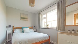 Un dormitorio con una cama de madera, mesitas de noche, un aparador, una ventana con cortinas y un cuadro de un paisaje urbano en la pared.
