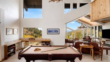 A spacious room with a pool table, comfortable seating, and large windows offering a view of the outdoors.