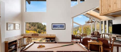 A spacious room with a pool table, comfortable seating, and large windows offering a view of the outdoors.
