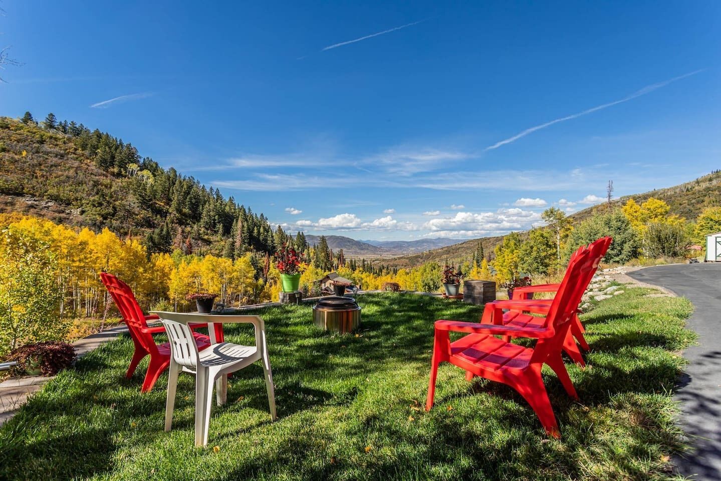 A grassy outdoor area with red and white chairs, a table, and potted plants.
