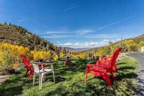 A grassy outdoor area with red and white chairs, a table, and potted plants. - Private Luxury Mountain Estate w/ Views & Hot Tub (Steamboat Springs)