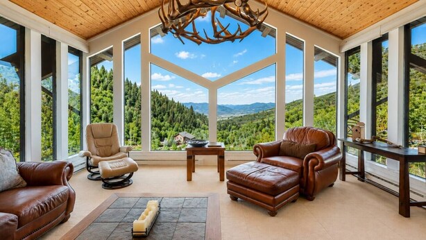 A spacious room with leather sofas, a coffee table, and a large window offering a view of a forested landscape. - Private Luxury Mountain Estate w/ Views & Hot Tub (Steamboat Springs)