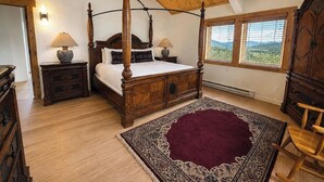 A four-poster bed with a wooden headboard, two bedside tables with lamps, a large patterned rug, and a view of the outdoors through the windows. - Private Luxury Mountain Estate w/ Views & Hot Tub (Steamboat Springs)