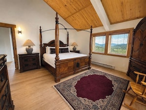 A four-poster bed with a wooden headboard, two bedside tables with lamps, a large patterned rug, and a view of the outdoors through the windows. - Private Luxury Mountain Estate w/ Views & Hot Tub (Steamboat Springs)