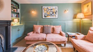 Un salon chaleureux avec un mur vert, un canapé rose, une bibliothèque et une cheminée.