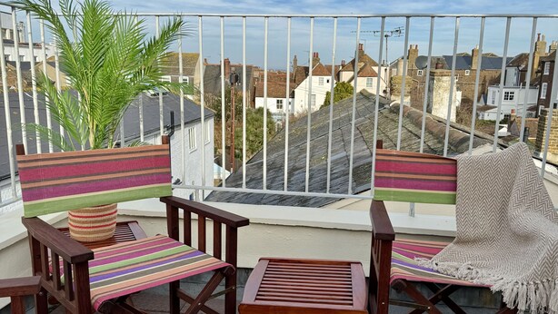 Un balcon avec des chaises en bois et une table, une tasse blanche et des biscuits sur la table.