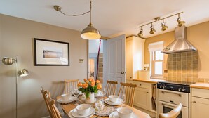 Un coin repas avec une table en bois dressée pour quatre personnes, un vase de fleurs et une cuisine équipée d’une cuisinière et d’un four.