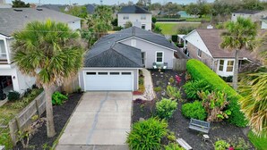 A residential area with houses, a driveway, and a well-maintained garden with various plants and a palm tree. - Pool Home Walk to Beach | Good Morning Rentals (Jacksonville Beach)