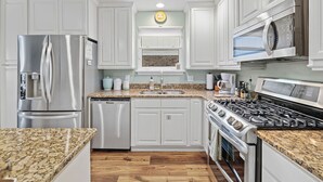 A modern kitchen with white cabinets, stainless steel appliances, granite countertops, and a central island. - Pool Home Walk to Beach | Good Morning Rentals (Jacksonville Beach)