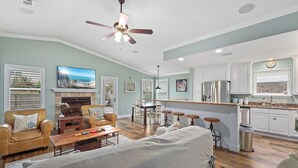A spacious living room with a fireplace, a dining area, and a kitchen with white cabinets and a bar. - Pool Home Walk to Beach | Good Morning Rentals (Jacksonville Beach)