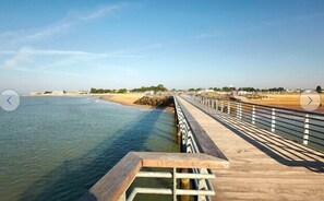 A wooden boardwalk extending over a body of water, with a railing on one side and a sandy beach on the other.