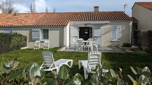 Ein Haus mit Ziegeldach, einer Haustür und einer Terrasse mit weißen Plastikstühlen und einem Tisch.