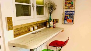 A kitchen with a white countertop, two bar stools, a vase with flowers, and a poster on the wall. - SHINE CHALET - UNIQUE & COMFORTABLE ACCOMMODATION (REDRUTH)