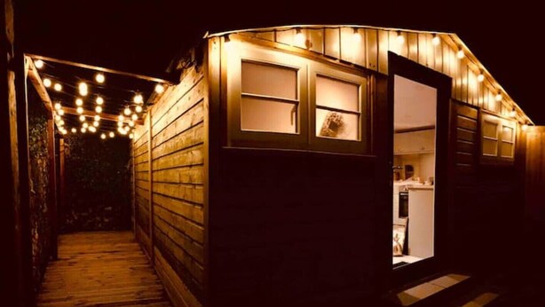 A wooden cabin with a wooden staircase leading to a door, illuminated by string lights. - SHINE CHALET - UNIQUE & COMFORTABLE ACCOMMODATION (REDRUTH)