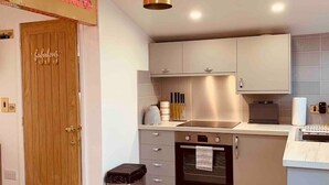 A modern kitchen with white cabinets, a stainless steel oven, and a wooden door. - SHINE CHALET - UNIQUE & COMFORTABLE ACCOMMODATION (REDRUTH)