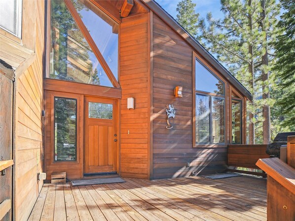 A wooden cabin with large windows, a wooden deck, and a mountain backdrop.