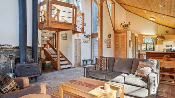 Ein gemütliches Wohnzimmer mit Kamin aus Stein, einer Holztreppe und einem bequemen Sofa.