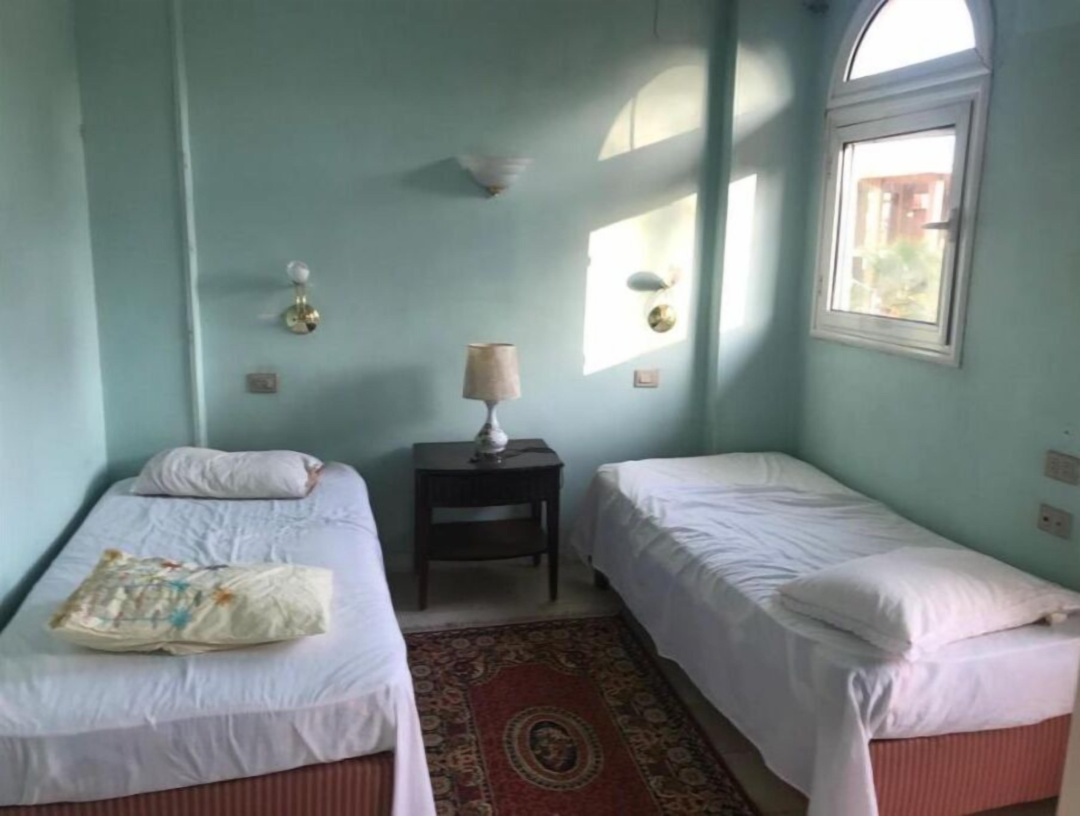 Une chambre avec deux lits simples, une petite table avec une lampe et un tapis à motifs.