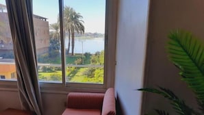 Una habitación con un ventanal grande, un sofá a rayas, una mesita y una planta en maceta.