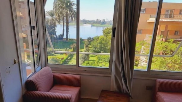 Una habitación con dos sofás a rayas, una pequeña mesa de madera y un ventanal con vistas a un lago y vegetación.