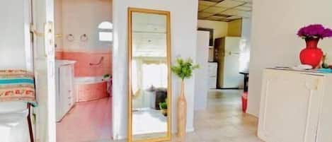 A spacious hallway with a large mirror, a potted plant, and a red vase on a cabinet.