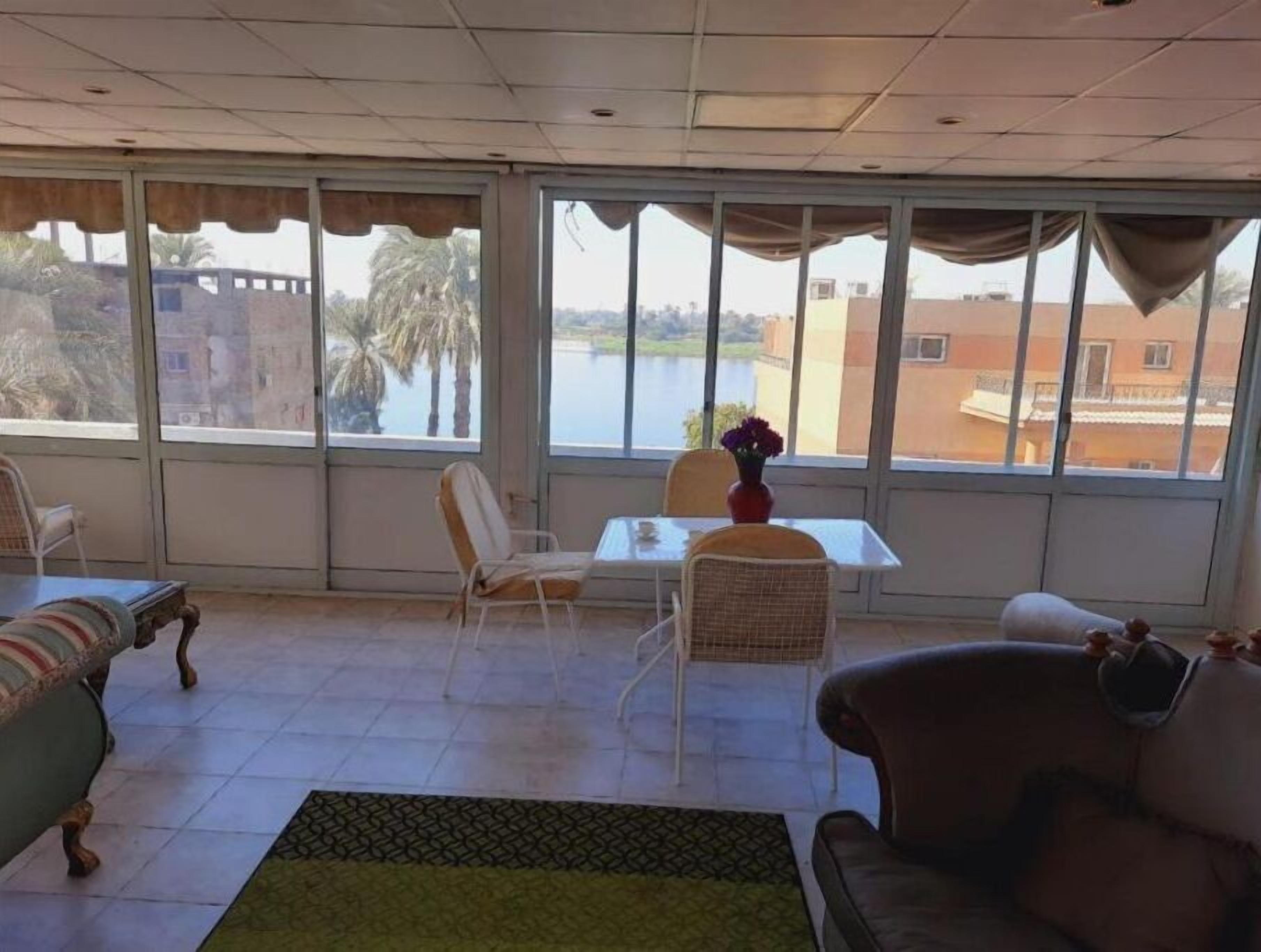 A room with a dining table and chairs, a sofa, and a view of a body of water and buildings.