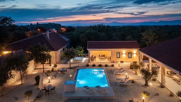 Un resort con piscina, mobiliario exterior y vistas a la montaña al anochecer.