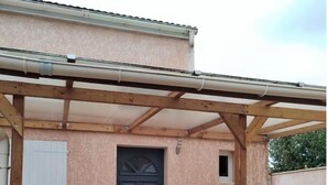 Ein überdachter Patio-Bereich mit einer Holzw pergola, einer schwarzen Tür und einem kleinen Tisch mit Stühlen.