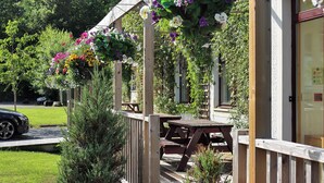 A wooden deck with hanging flower baskets, a wooden fence, and a building with a visible door and window.
