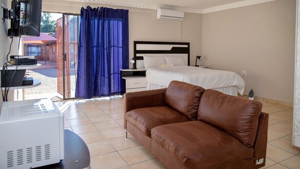 Habitación de hotel con sofá de cuero marrón, cama con ropa blanca, escritorio pequeño con una computadora y televisor montado en la pared.