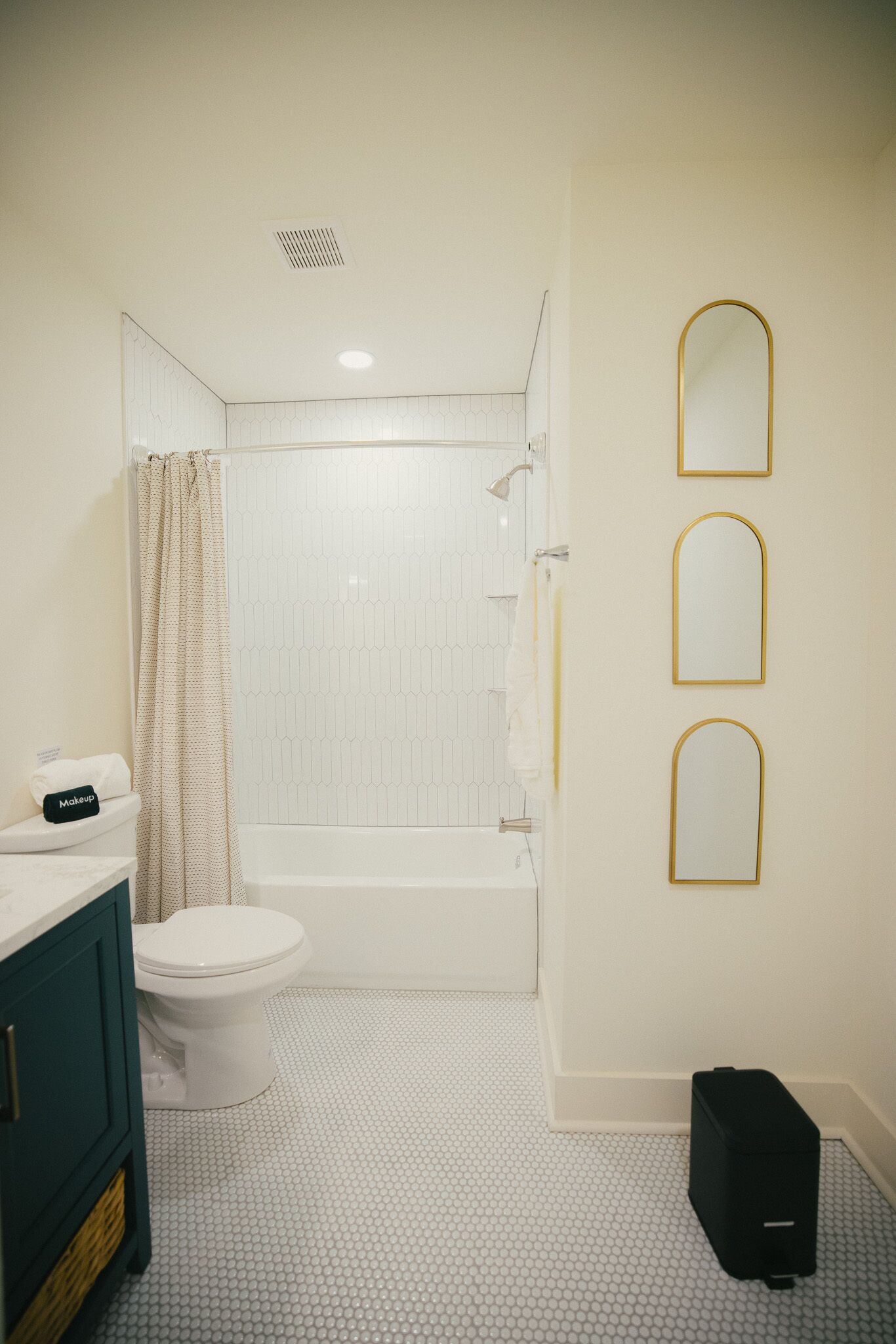 A bathroom with a toilet, bathtub, and shower curtain. There are three mirrors on the wall and a black suitcase on the floor.