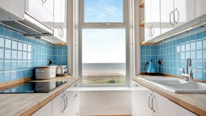Una cocina con vista a la playa, armarios blancos, azulejos azules y una ventana.