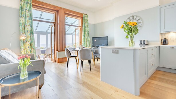 Una cocina moderna con una isla central, un comedor con sillas y una sala de estar con un sofá y una mesita de centro.