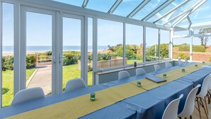 Un invernadero con mesa puesta para comer, ventanas amplias y vista al mar.