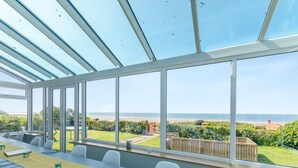 Una habitación con una mesa larga, sillas y ventanas amplias con vista a una playa.
