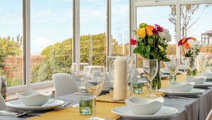 Una mesa de comedor dispuesta con platos, tazones y vasos blancos, con un jarrón de flores en el centro.
