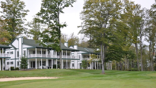 A multi-story building with a porch, surrounded by a well-maintained lawn and trees. - Fairway to Heaven at Shanty Creek (Bellaire)