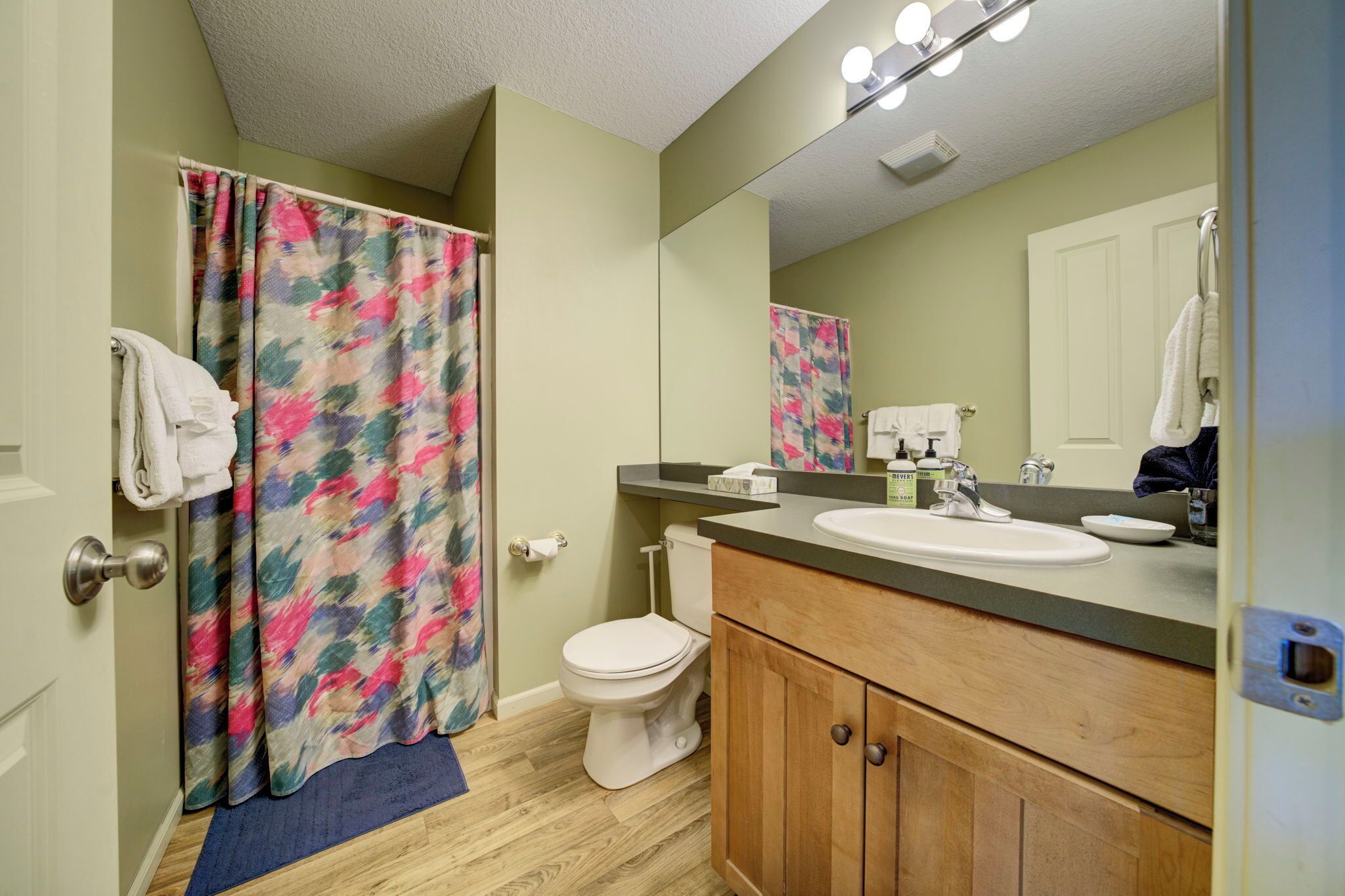 A bathroom with a shower curtain, toilet, sink, and mirror.