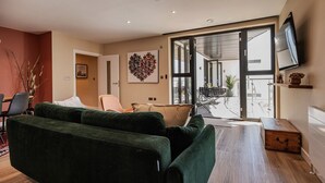 Un salon moderne avec un canapé vert, une table basse en bois et une grande fenêtre donnant sur l’extérieur.