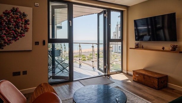 Un salon moderne doté d’une grande porte-fenêtre coulissante donnant sur un balcon avec vue sur la plage.