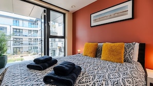 Une chambre d’hôtel avec un grand lit, une vue à travers une porte vitrée et un tableau encadré au mur.