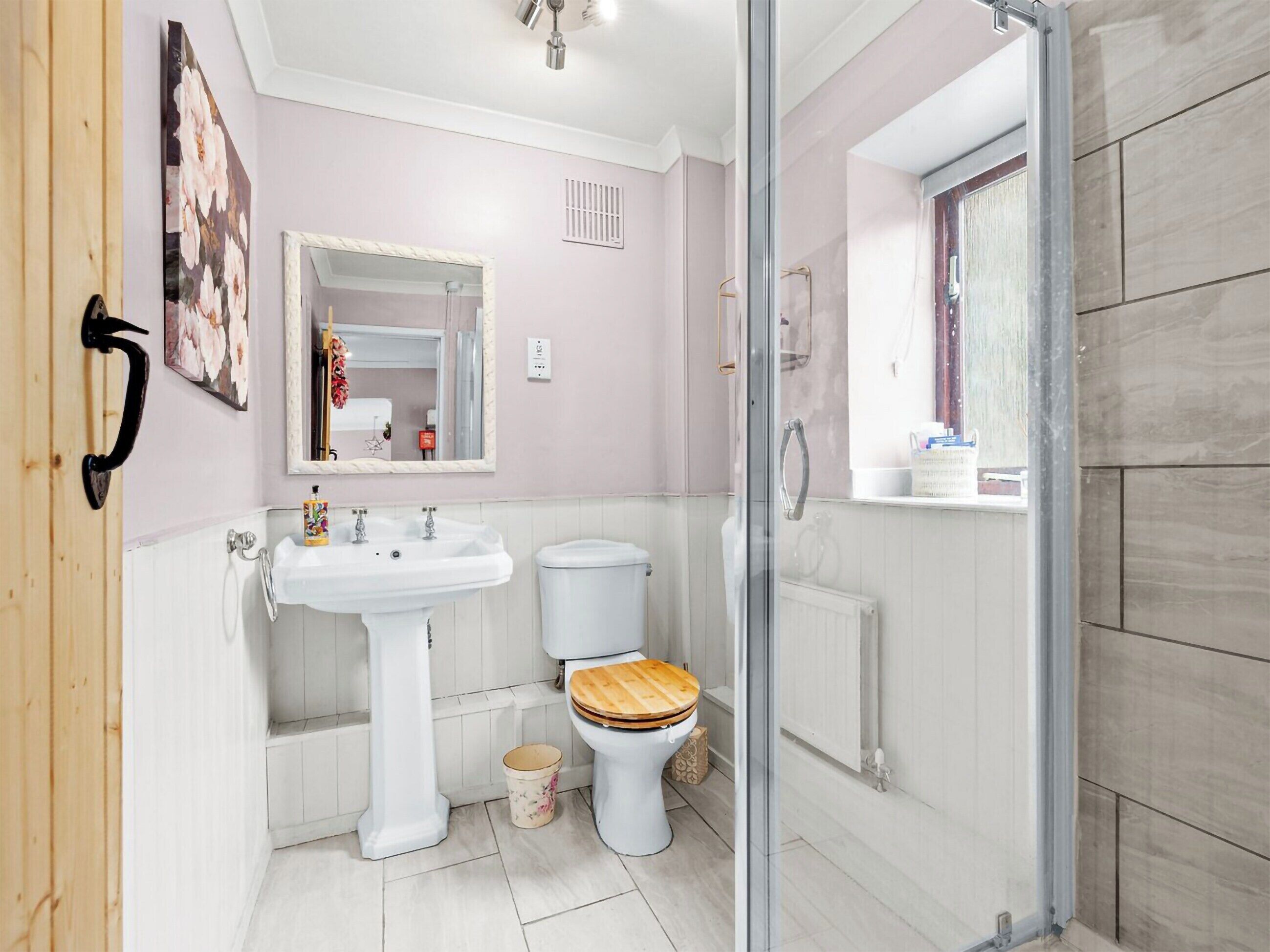Een badkamer met een wastafel op voetstuk, toilet en een douchecabine met glazen wanden.
