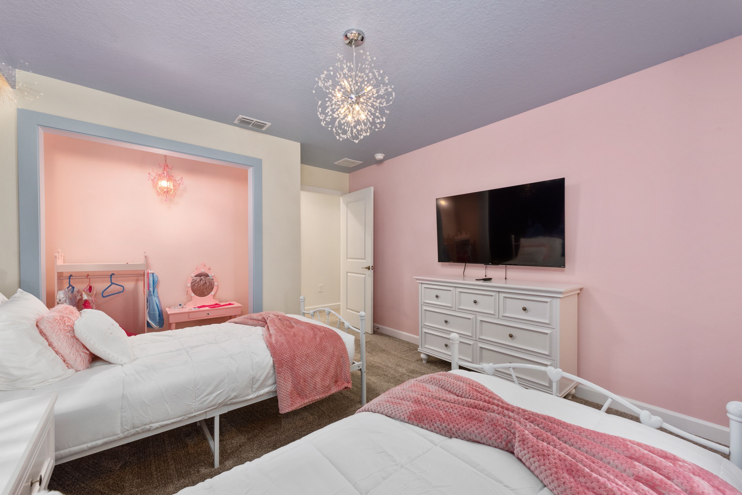 A bedroom with two beds, a dresser, a TV, and a chandelier.