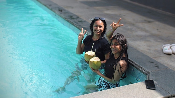 Deux personnes dans une piscine, tenant des noix de coco et faisant le signe de la paix.