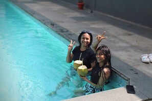 Two people in a swimming pool holding coconuts and making peace signs.