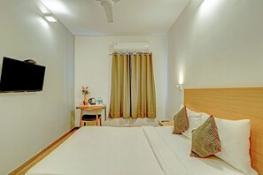 Habitación de hotel con cama, escritorio con silla, televisión y ventana con cortinas.